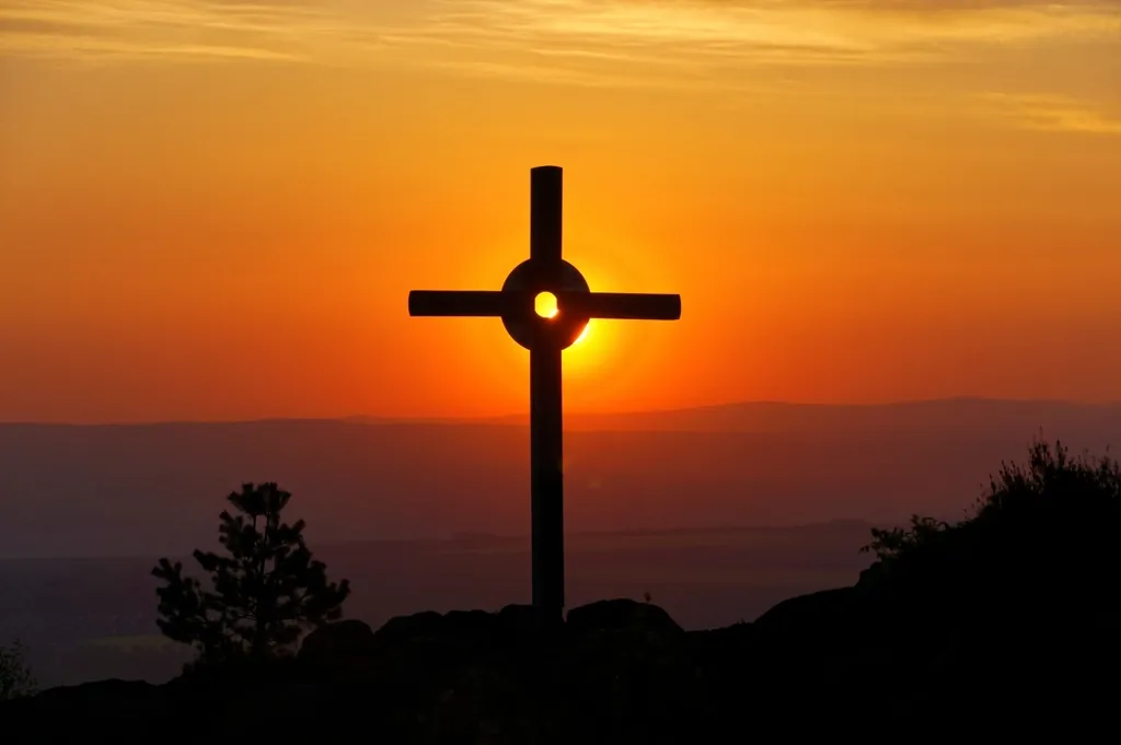 A wooden cross on a hilltop at sunset